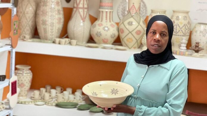 Artist Zenab Grabia holds one of her art pieces, a ceramic dish with colorful art.