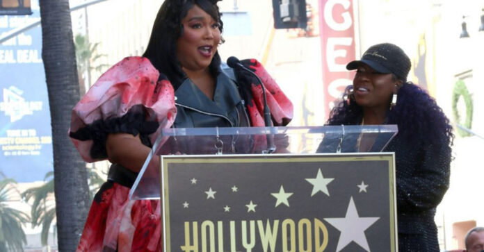 A photo of Lizzo, the singer, speaking at a podium with Missy Elliot Standing next to her
