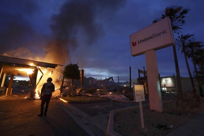 A man looks on as a bank burns after a protest over the death of George Floyd, on May 31, 2020, in La Mesa, Calif. A former San Diego-area police officer who pushed a Black man during an arrest in 2020 was acquitted Friday, Dec. 10, 2021, of lying on his report about the incident, which was captured on video and sparked widespread looting and arson amid nationwide racial unrest